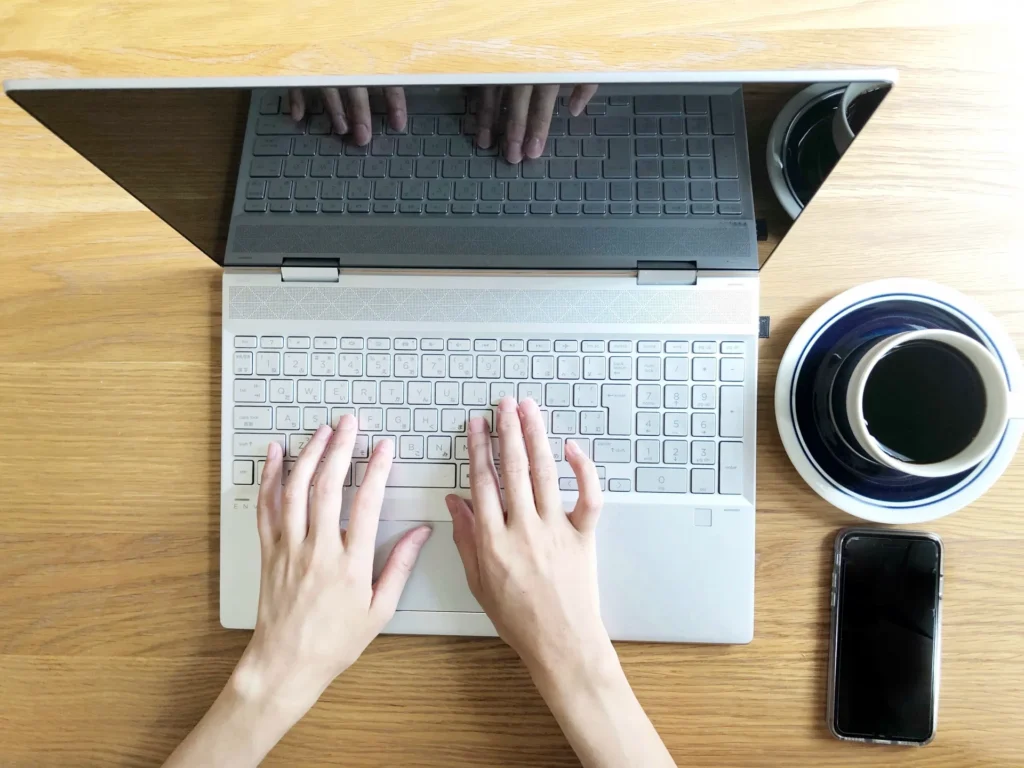 珈琲とスマホを置いて、ノートパソコンで作業する様子