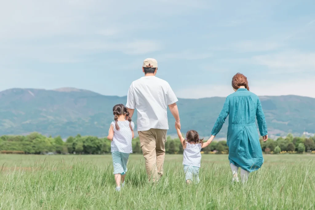 手を繋ぎ草原を歩く家族（後ろ姿）