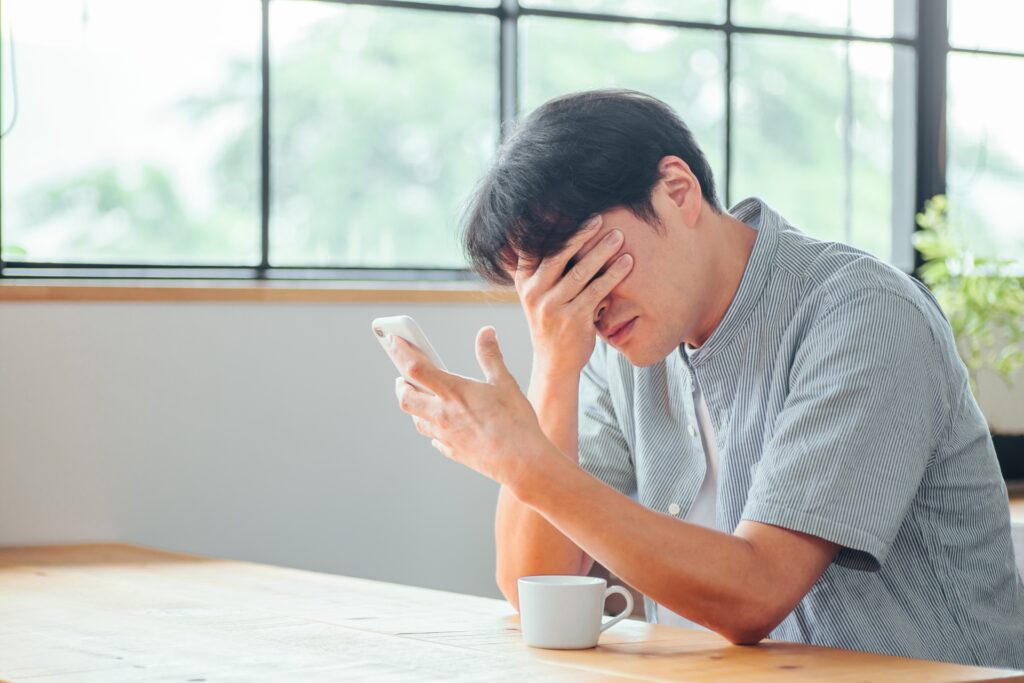 スマートフォンを片手に手で目元を覆い隠している男性