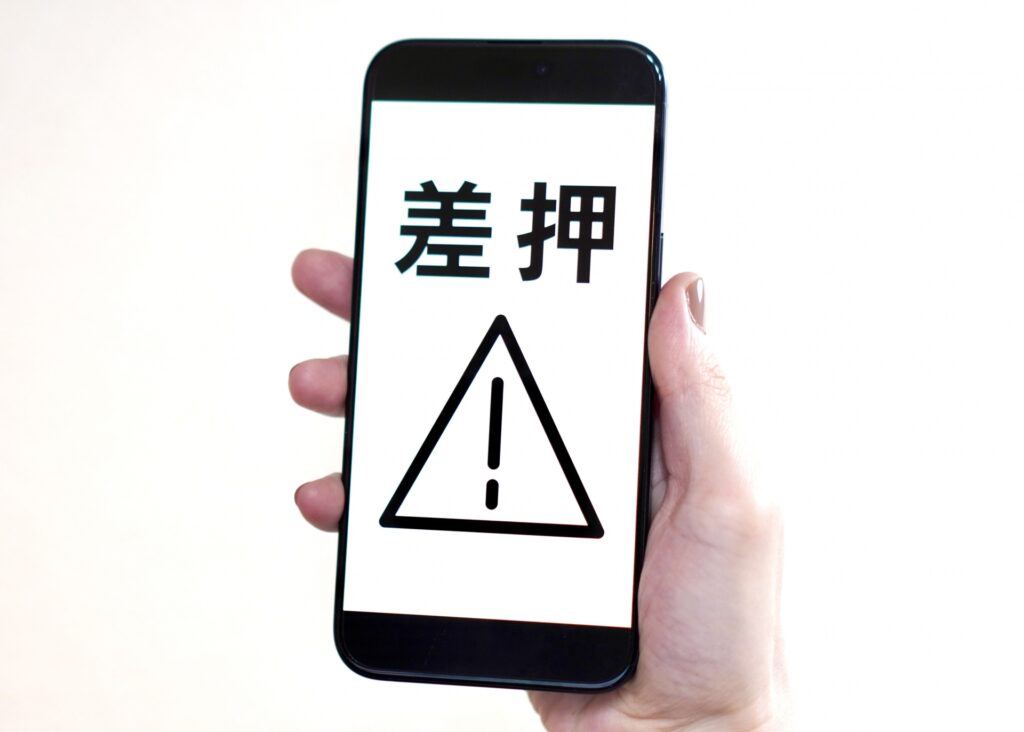 スマートフォンに「差し押さえ」と書かれた画面を見せている